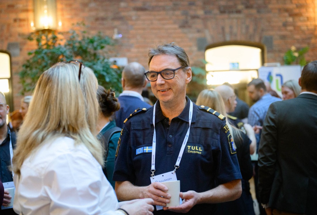 En tullinspektör ler och pratar med en person i vit skjorta.