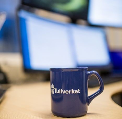 Tullverkets kaffekopp med en skärm i bakgrunden.